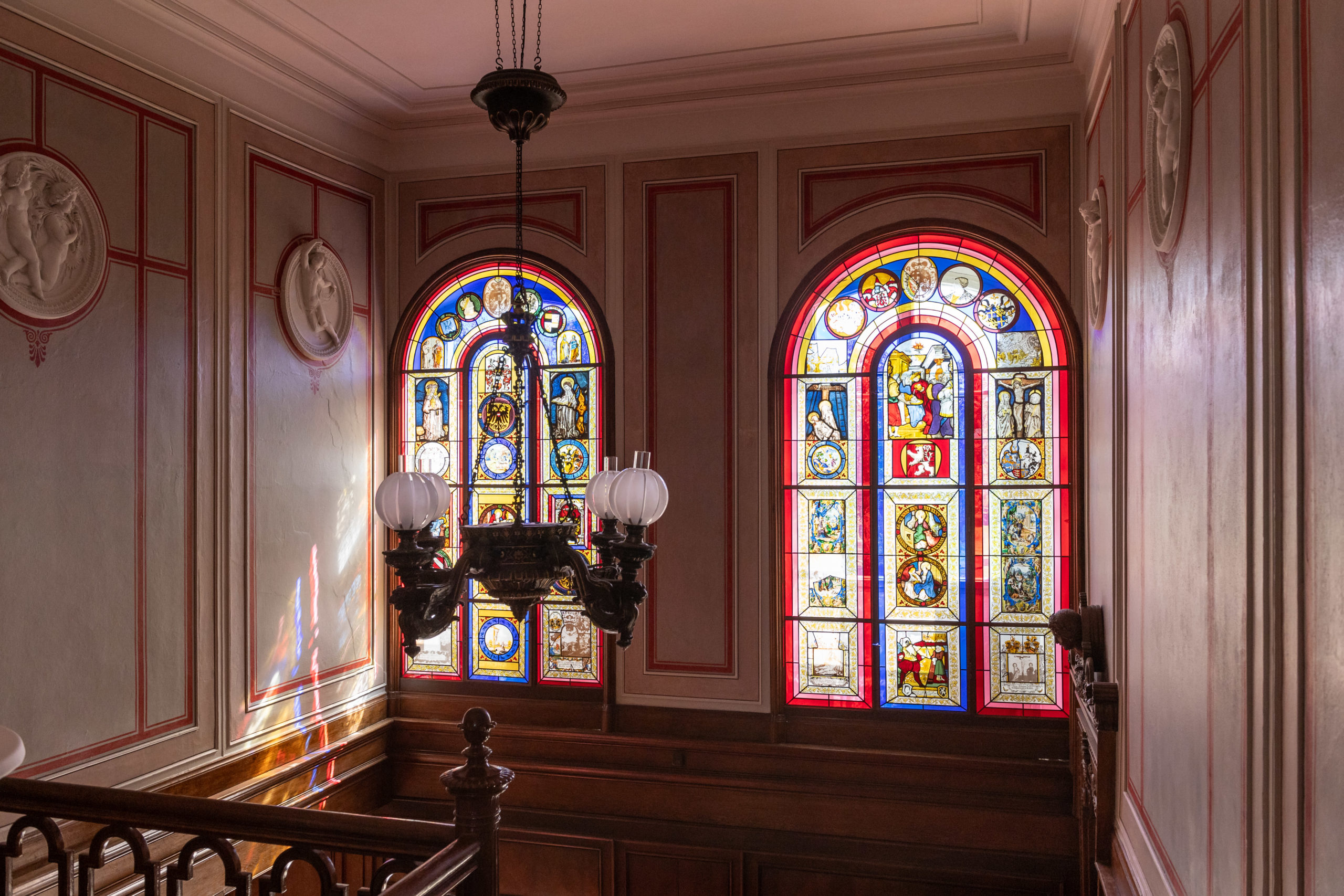 zwei Fenster mit verschiedenen bunten Glasmalereien im Treppenhaus von Schloss Branitz