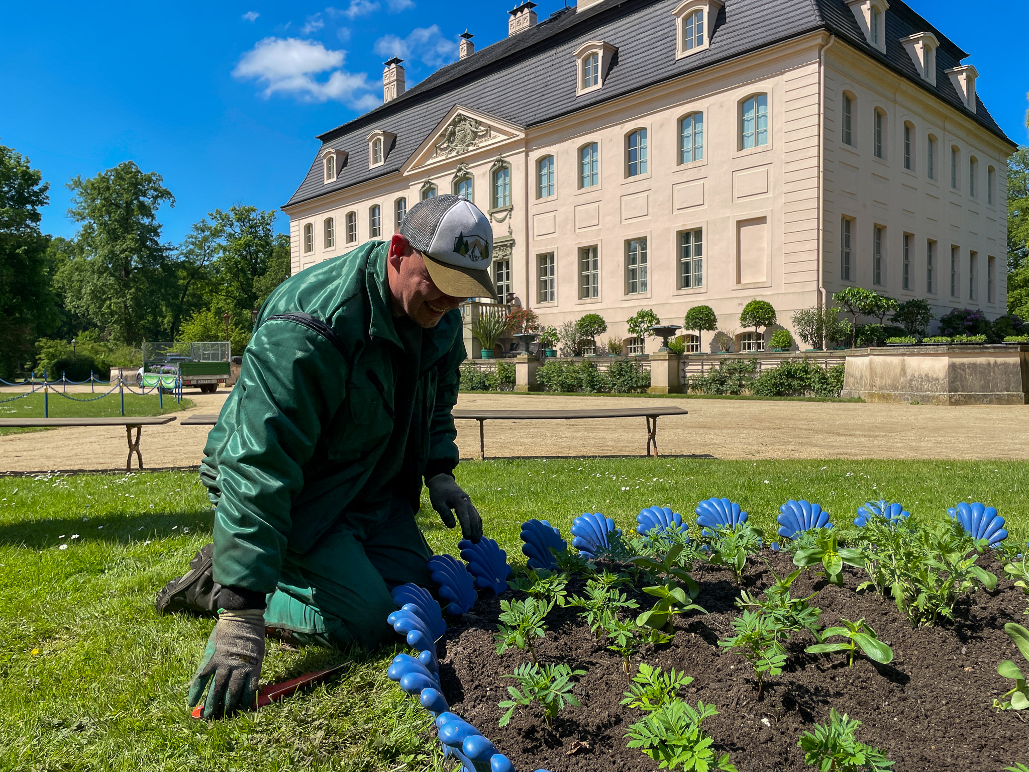 Ein Gärtner kniet vor einem Blumenbeet, das er gerade bepflanzt hat. Im Hintergrund ist Schloss Branitz.