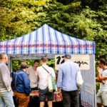 5 Männer stehen vor einem Verkaufszelt beim Branitzer Weinfest.