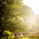 Auf einer Wiese vor dem Schloss Branitz sitzt eine Frau in einem Liegestuhl auf einer Wiese. Im Hintergrund schieben zwei Personen ihre Fahrräder.